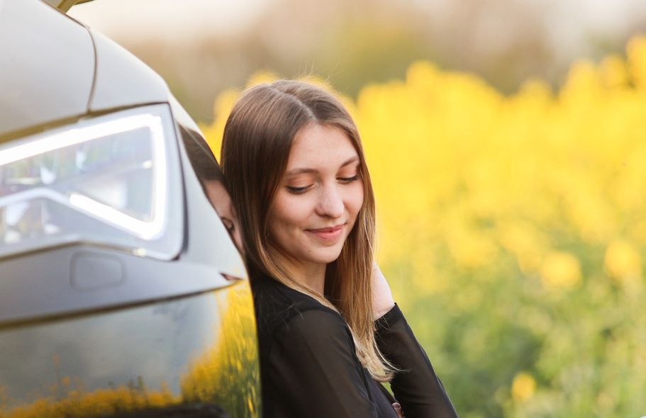 Model lehnt an Auto, im Hintergrund blühender Raps.